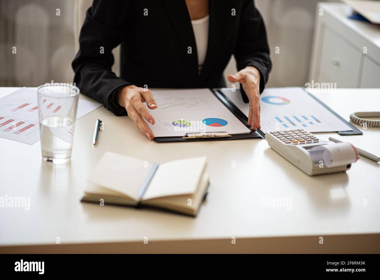 Geschäftsfrau, die an ihrem Schreibtisch sitzt und an einem Finanzbericht mit Grafiken und Diagrammen arbeitet. Stockfoto