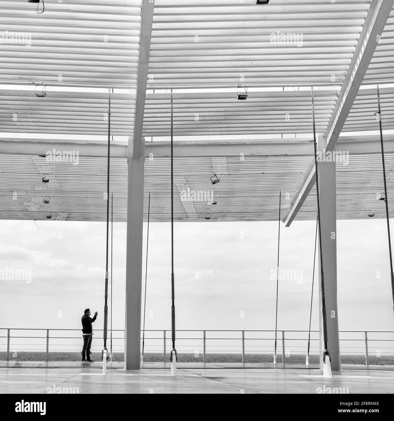 Malaga, Andalusien, Spanien. 02/08/2021. Mann, der an einem bewölkten Tag aus Stahl und Glas vor dem Meer fotografiert. Stockfoto