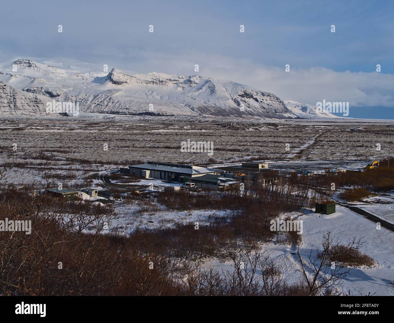 Schöne Luftaufnahme des Besucherzentrums Skaftafellsstofa im Vatnajökull Nationalpark im Winter mit den zerklüfteten, schneebedeckten Bergen von Öræfajökull. Stockfoto