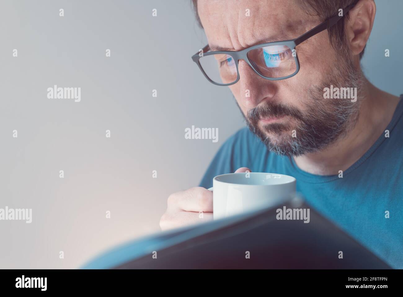Headshot Portrait of Mid-adult Male with Brillen leading a book and Drinking Coffee at Home, closeup with selective Focus Stockfoto