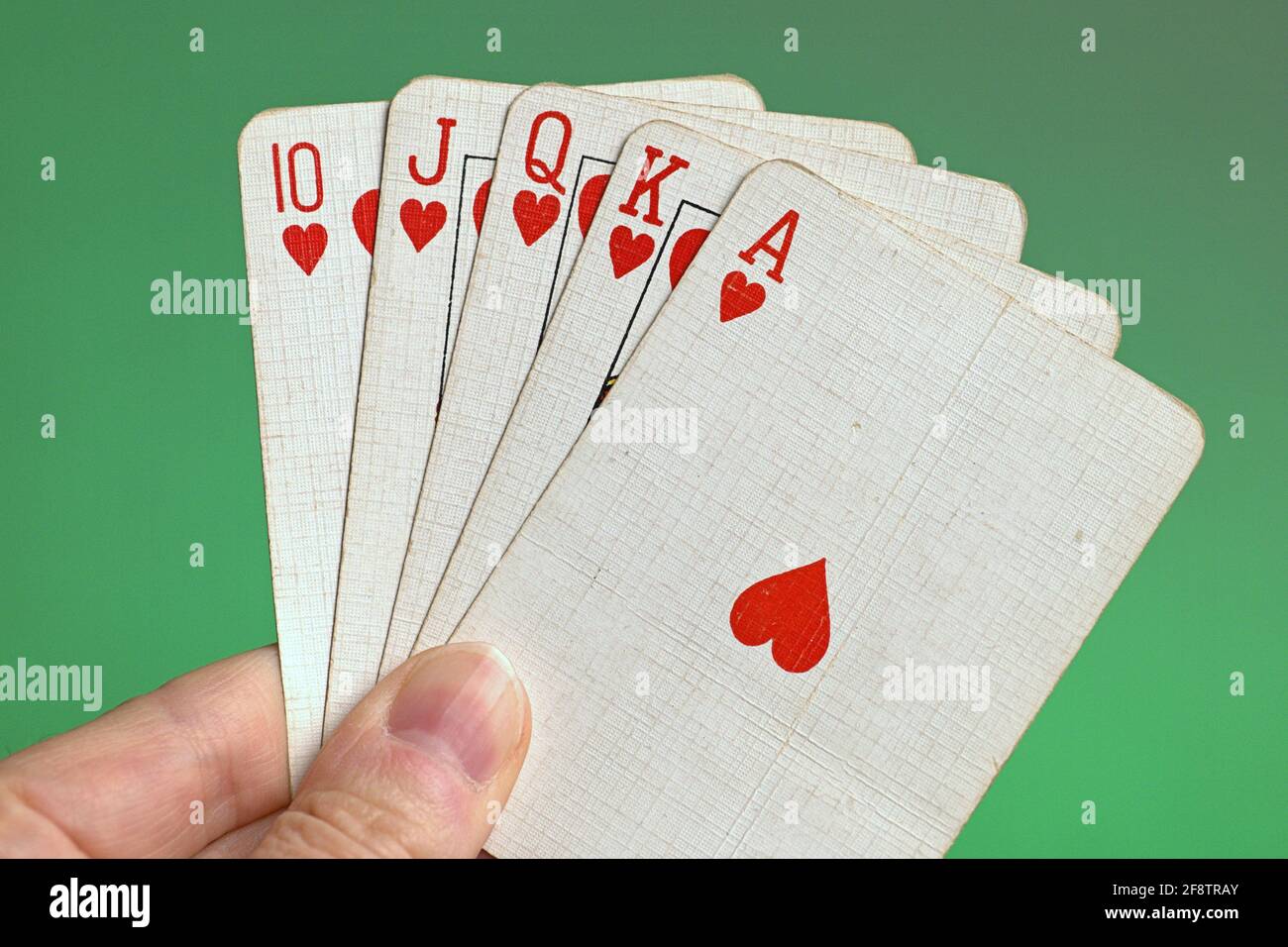 Deutschland. April 2021. Spielen von Karten einer Pokerhand aus einem alten Kartenspiel, Französisch Hand, mit einem Royal Flush, der höchste Straight Flush im Poker, bestehend aus zehn, Bube, Dame, König und Ass von einer Farbe, gehalten von einer Hand im Tor vor einem grünen Hintergrund. Credit: dpa/Alamy Live News Stockfoto