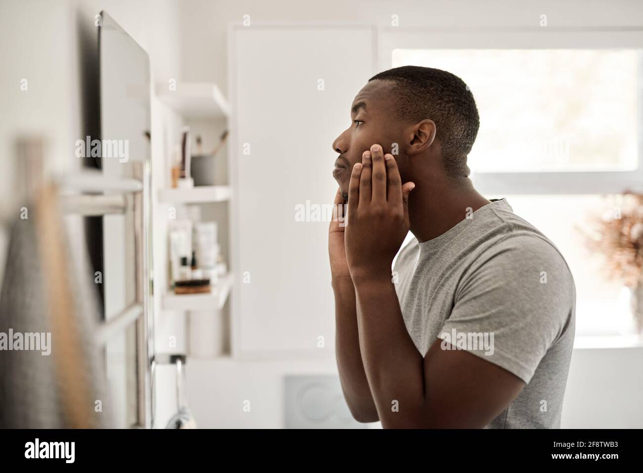 Der junge Afrikaner untersucht seinen Teint in seinem Badezimmer Stockfoto