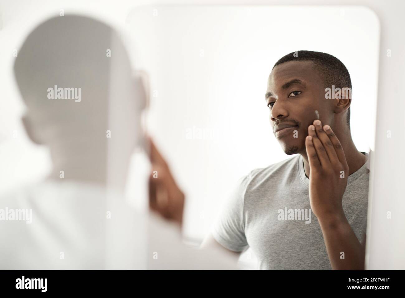 Afrikanischer Mann, der in seinem Badezimmer Lotion auf sein Gesicht aufgetragen hat Spiegel Stockfoto