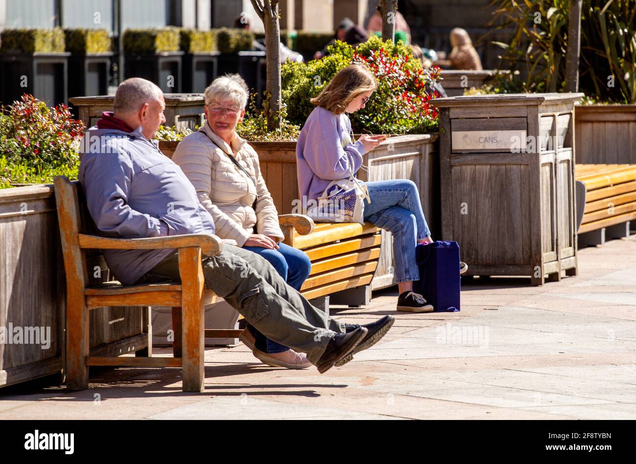 Dundee, Tayside, Schottland, Großbritannien. April 2021. UK Wetter: Ein sonniger Morgen mit einer leichten kühlen Brise über Nordostschottland mit Temperaturen bis zu 12 Grad Die Sperrung von Covid-19 wird durch das Einkaufen von Menschen im Stadtzentrum von Dundee gelockert, da in der Hauptstraße einige wichtige Einzelhandelsgeschäfte eröffnet werden. Eine junge Frau nutzt die neuen lockeren Sperrbestimmungen und das sonnige Aprilwetter, um auf den Sommersitzen auf dem City Square zu sitzen und nach einem Einkaufstag Nachrichten auf ihrem Smartphone zu schreiben. Kredit: Dundee Photographics/Alamy Live Nachrichten Stockfoto