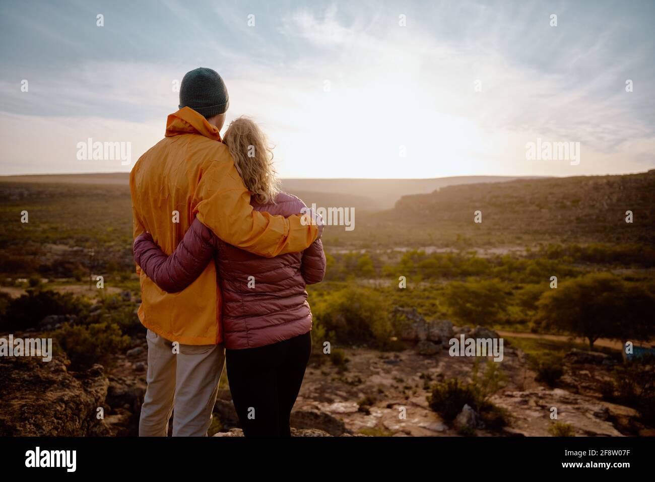 Rückansicht eines jungen Paares, das sich beim Schauen verliebt Bei schönem Sonnenaufgang nach dem Wandern zum Rand der Bergklippe Stockfoto