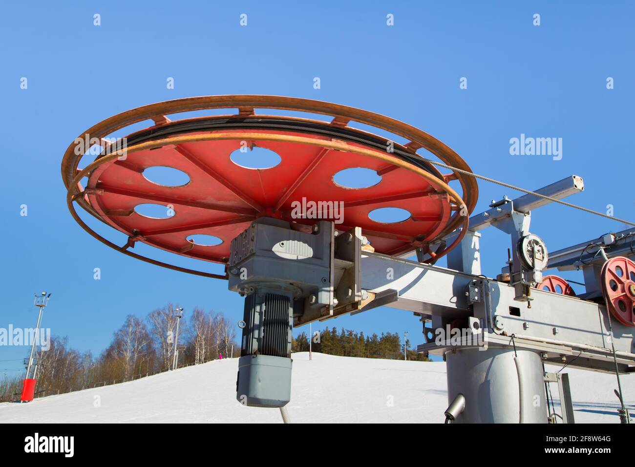 Großes Spinnrad mit Elektroseilzug-Motor in einem Skigebiet. Der Antriebsmechanismus gegen den blauen Himmel. Berghang Ausrüstung für Snowboarden. Skitouren an einem sonnigen Tag. Stockfoto