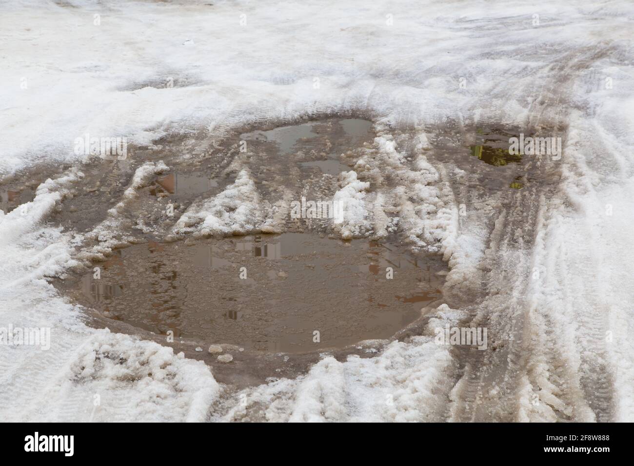 Autorad- und Reifenspuren auf einer kleinen Pfütze aus geschmolzenem Schnee. Abnormales Wetterkonzept. Es ist Speicherplatz für Kopien vorhanden. Das neue Jahr und die Weihnachtsfeiertage sind vorbei. Reste des Schnees vom letzten Jahr. Stockfoto