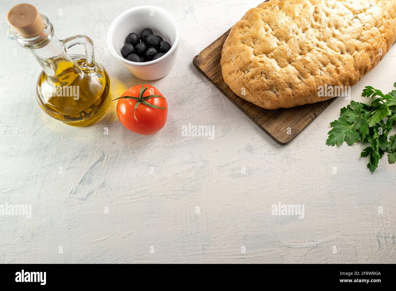 Italienisches Focaccia oder italienisches Brot.frisches, leckeres Brot mit aromatischen Kräutern auf Holzbrett neben schwarzen Oliven, Tomaten, Petersilie und Olivenöl auf Weiß Stockfoto