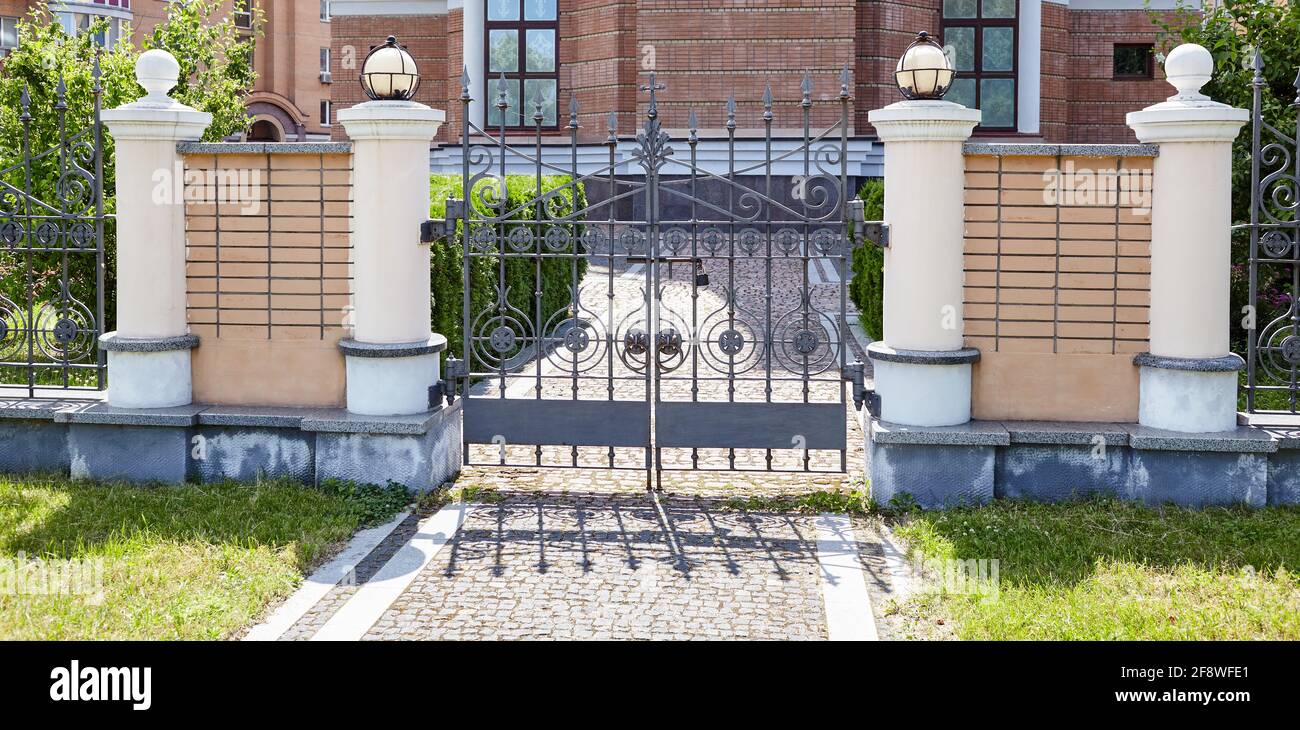 Schmiedeeiserne Tore für einen Tempel oder eine Kirche. Bild von einem schönen dekorativen gusseisernen schmiedeeisernen Zaun und Tore mit kunstvollen Schmieden und Steinsäulen Stockfoto