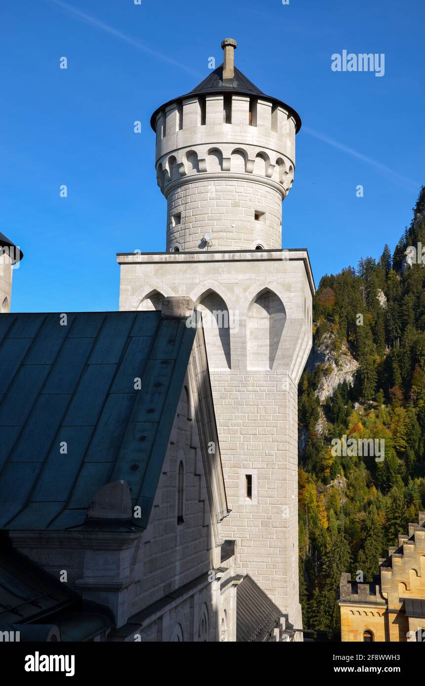 Einer der Türme des berühmten Schlosses Neuschwanstein mit Blauer Himmel und bewaldeter Berg im Hintergrund Stockfoto