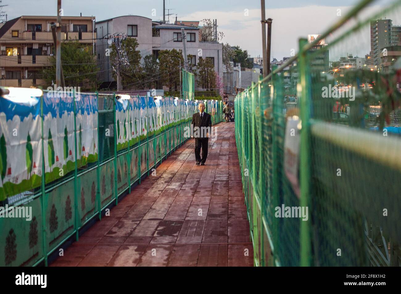 Ein älterer japanischer Salaryman mit schickem Business-Anzug, der bei Sonnenuntergang am Bausteg entlang läuft, Yamate Dori, Tokio, Japan Stockfoto