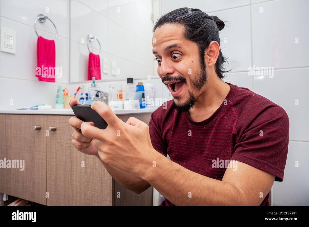 Ein junger lateinischer Mann lächelte auf der Toilette und benutzte ein  Smartphone im Badezimmer Stockfotografie - Alamy