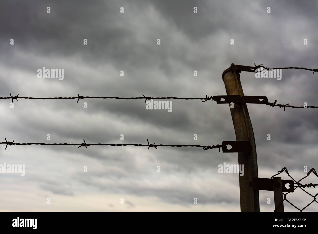 Zwei Reihen Stacheldraht und ein Zaunpfosten, mit Sturmwolken im Hintergrund. Einwanderungs-, Flucht- oder Freiheitskonzept. Stockfoto