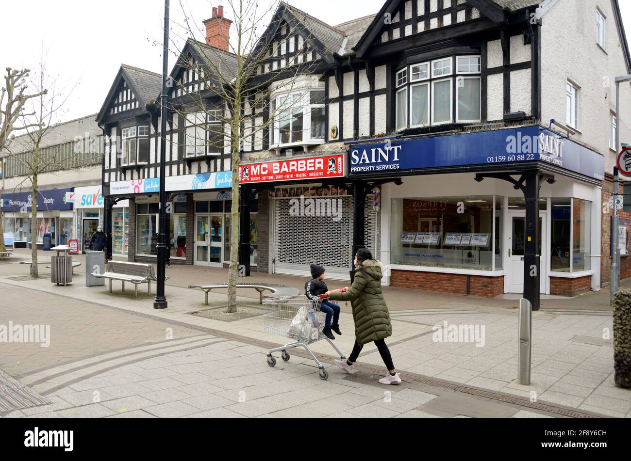 Frau in einem Anorak, die mit einem Kind einen Supermarkt-Trolley auf der Straße schiebt Stockfoto