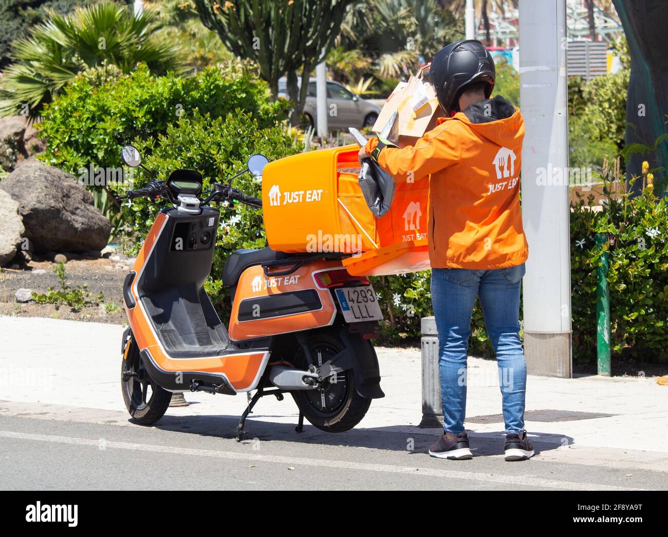 Essen Sie einfach Kurierfahrer in orangefarbener Uniform und essen Sie einfach Scooter/Motorrad in Spanien. Stockfoto