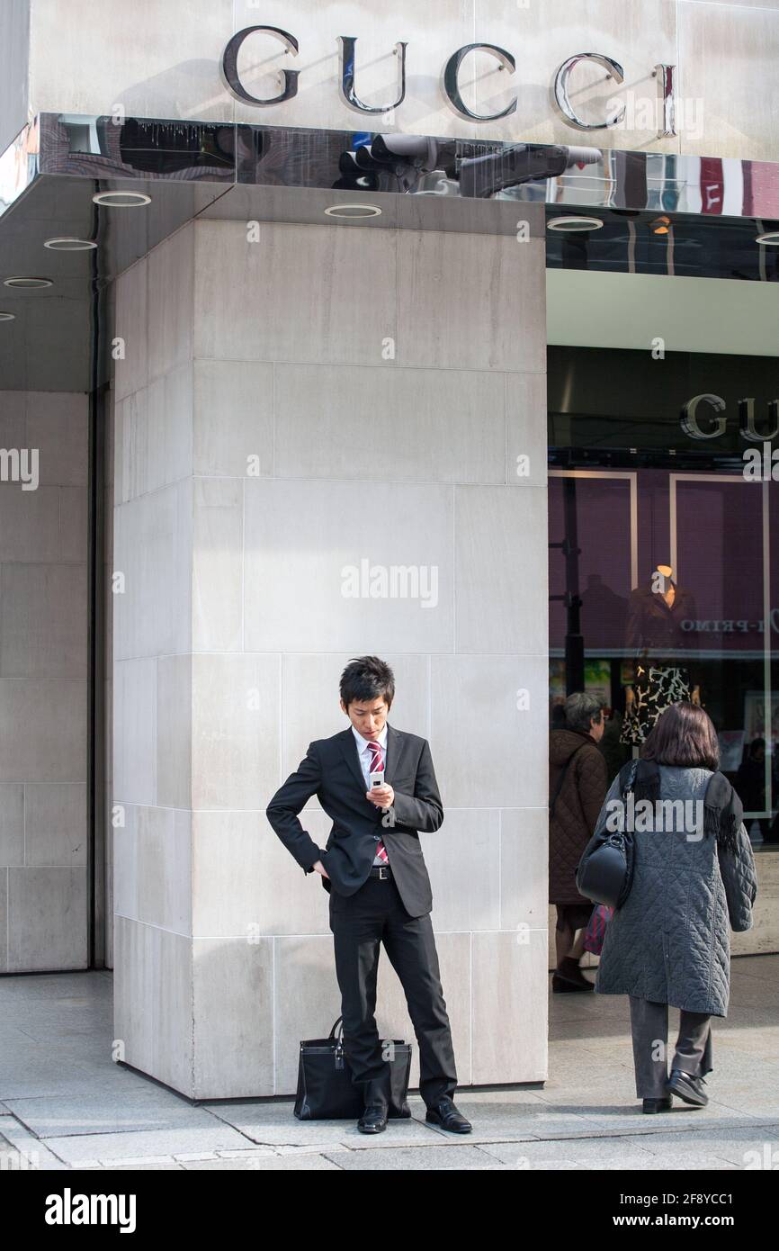 Der japanische Salaryman überprüft das Mobiltelefon, während er vor dem Gucci-Geschäft in Ginza, Tokio, Japan, wartet Stockfoto