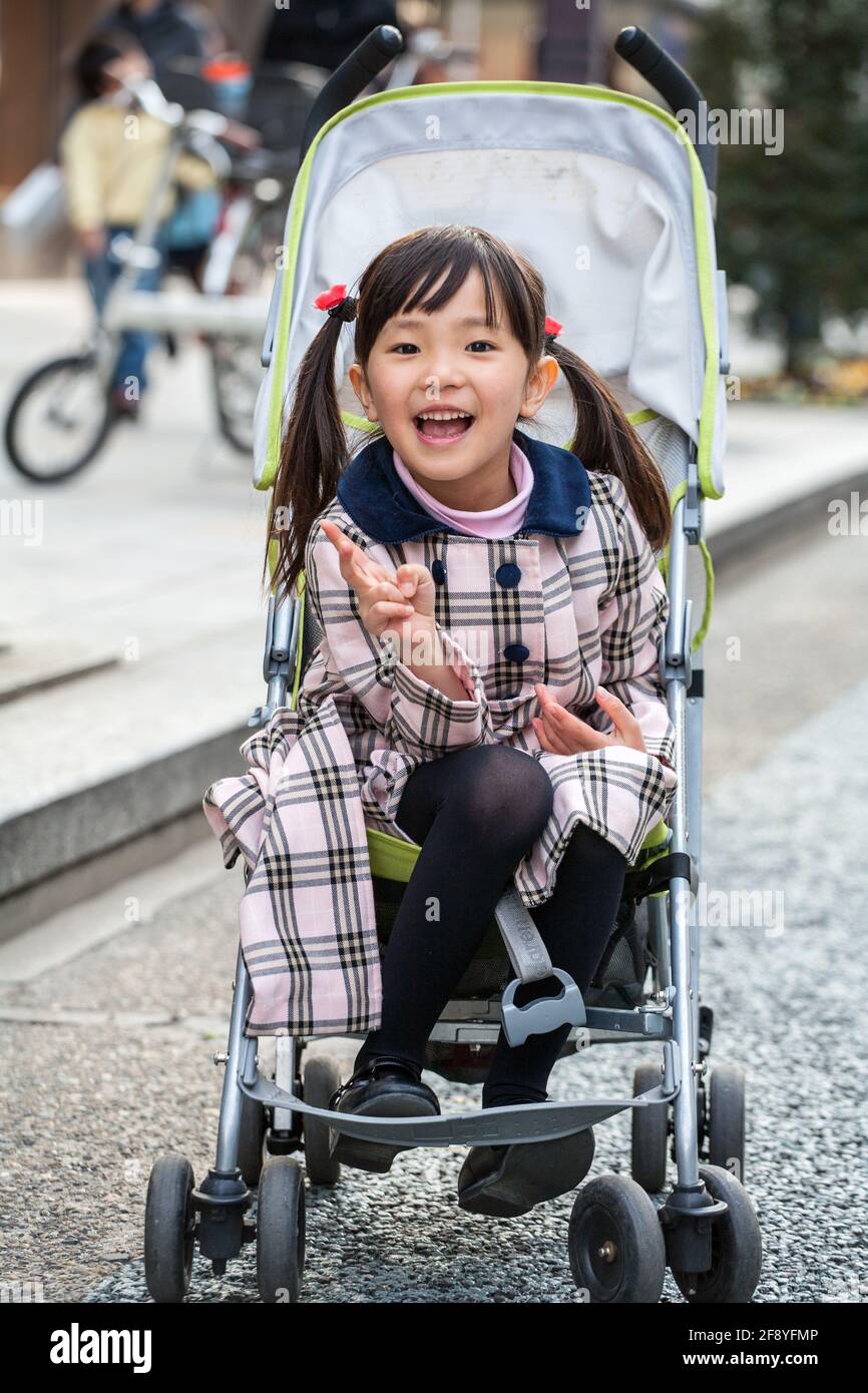 Das elegant gekleidete junge japanische Mädchen gibt V-Zeichen, das im  Kinderwagen der jüngeren Schwester, Ginza, Tokio, Japan, posiert  Stockfotografie - Alamy