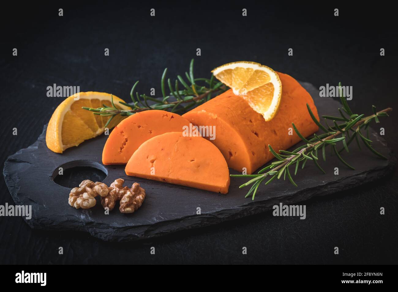 Halbrundes Stück Orangenkäse auf einem Schiefer, garniert mit Orange, Walnüssen und Rosmarin Stockfoto