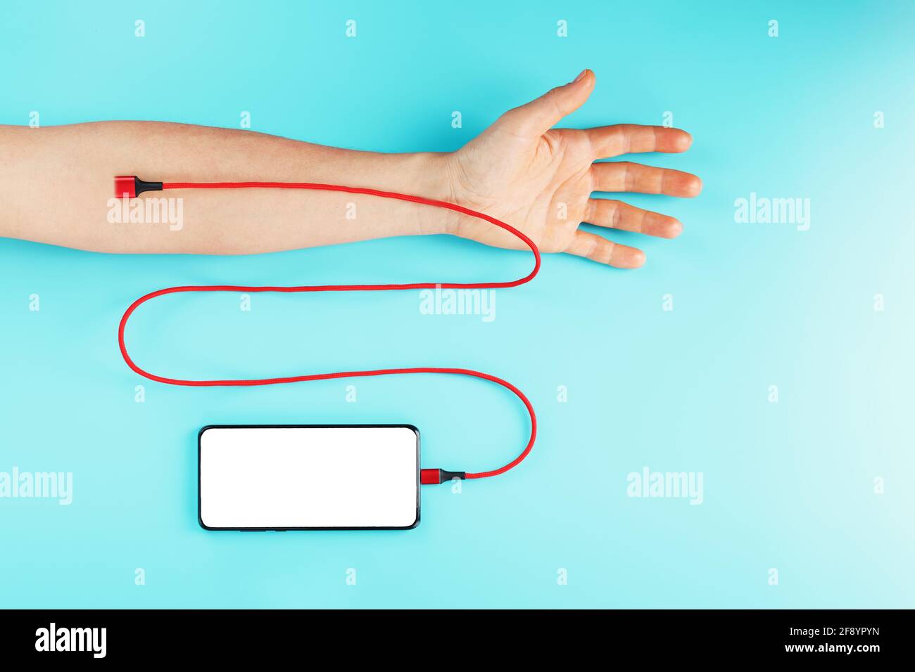 Die Hand wird über ein rotes Netzkabel mit einem Smartphone mit freiem Speicherplatz auf blauem Hintergrund verbunden. Das Konzept der Drogenabhängigkeit in den sozialen Netzwerken o Stockfoto