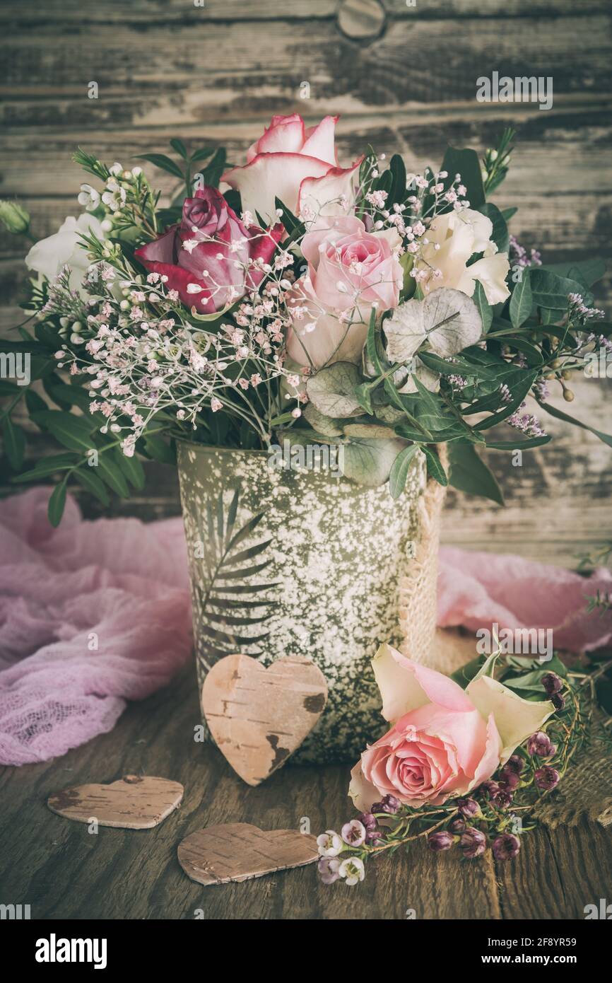 Vase mit Blumenstrauß mit rosa und weißen Rosen auf Holzhintergrund, Vintage-Stil, vertikal Stockfoto