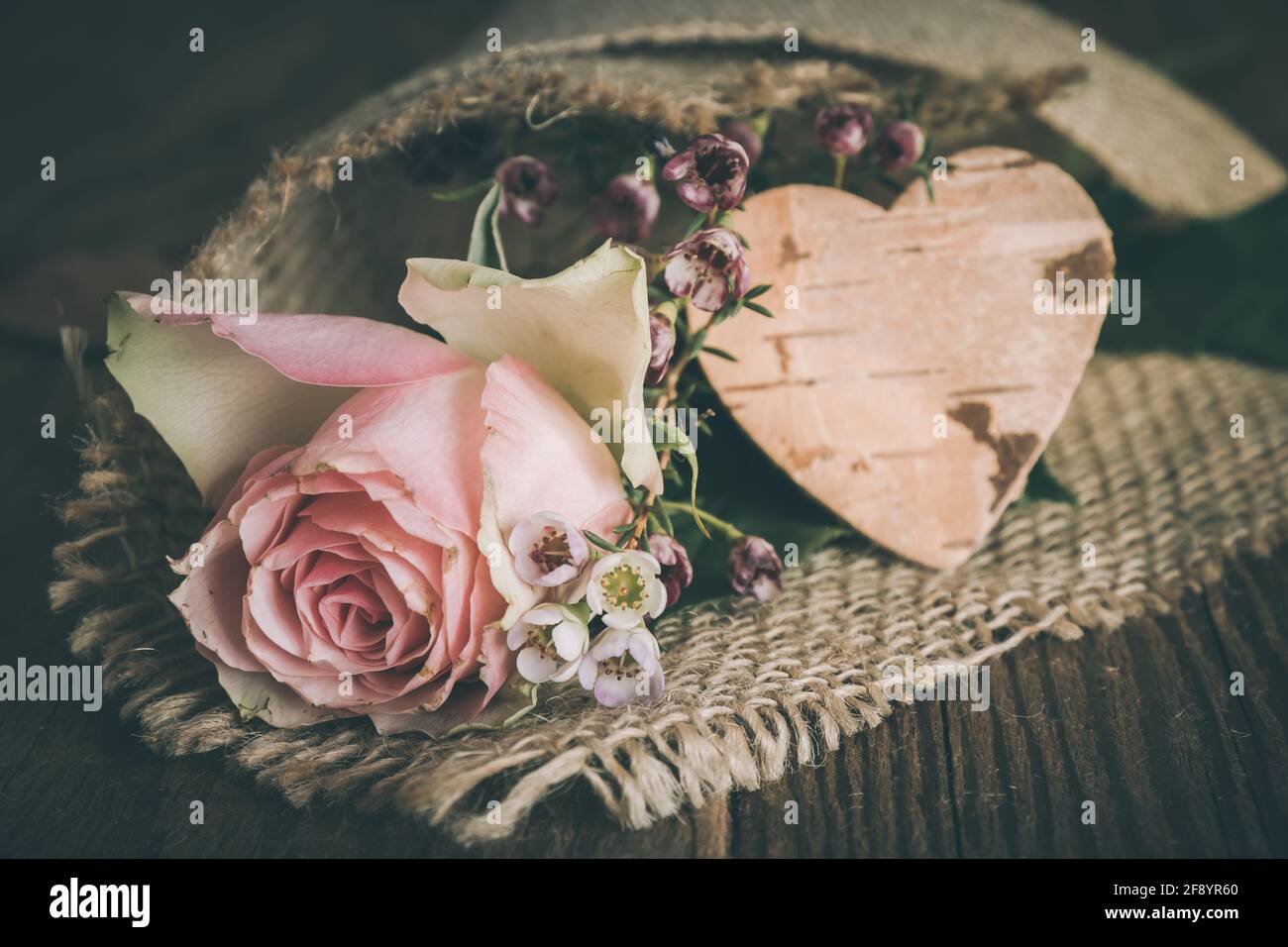 Rose und kleine Blumen in Jute zusammen mit einem eingewickelt Herz aus Baumrinde Stockfoto