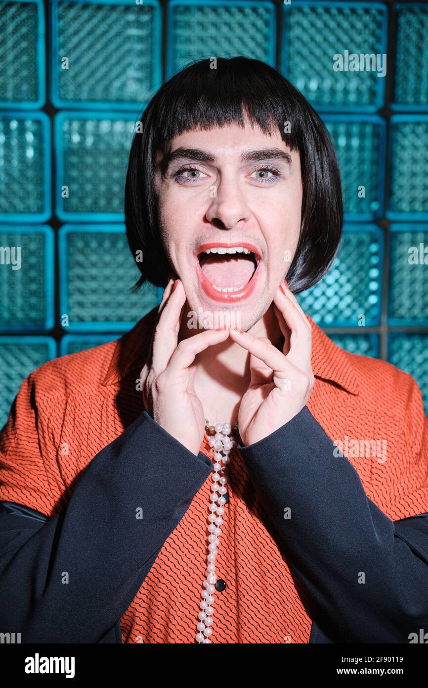 Porträt eines jungen Transgender mit rotem Lippenstift, der seinen Mund öffnet Und vor der Kamera posieren Stockfoto