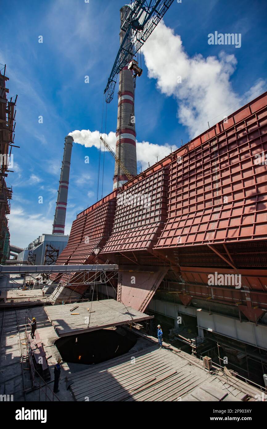 WÄRMEKRAFTWERK GRES-1. Modernisierung, Bau neuer riesiger Rohstoffkohlebunker. Kleine Leute unten. Rauchstapel auf dem Hintergrund. Ekibastuz. Stockfoto