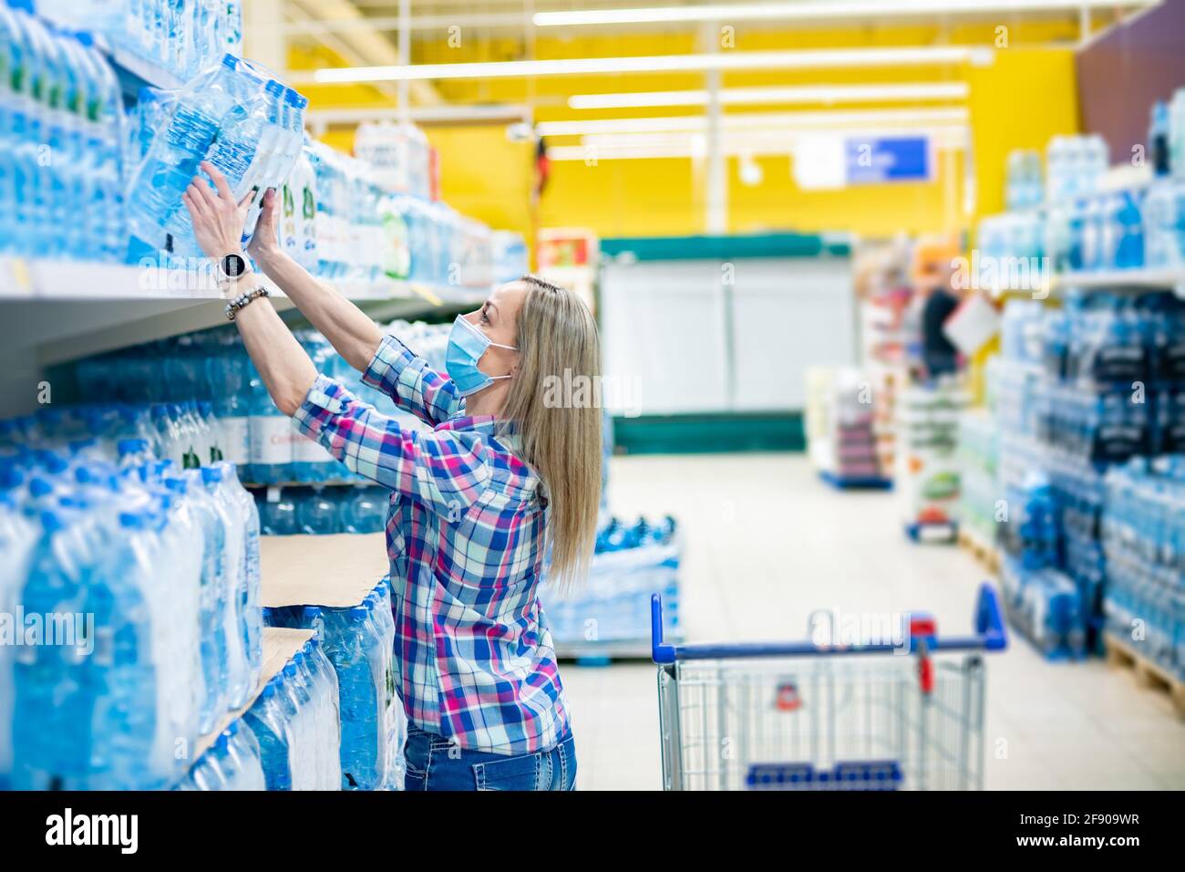 Frau in einer medizinischen Maske kauft sauberes Wasser in einem Supermarkt. Coronavirus-Pandemie. Stockfoto