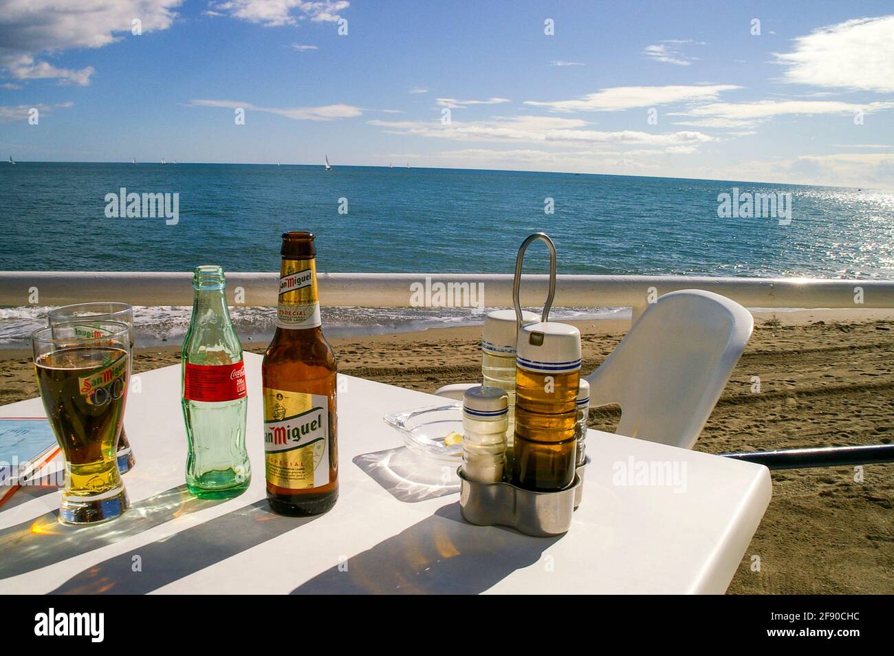 Authentisches, zufälliges Tischrestaurant am Strand in Fuengirola, Spanien, mit Blick auf das Mittelmeer. Flasche San Miguel Bier und Glas Stockfoto