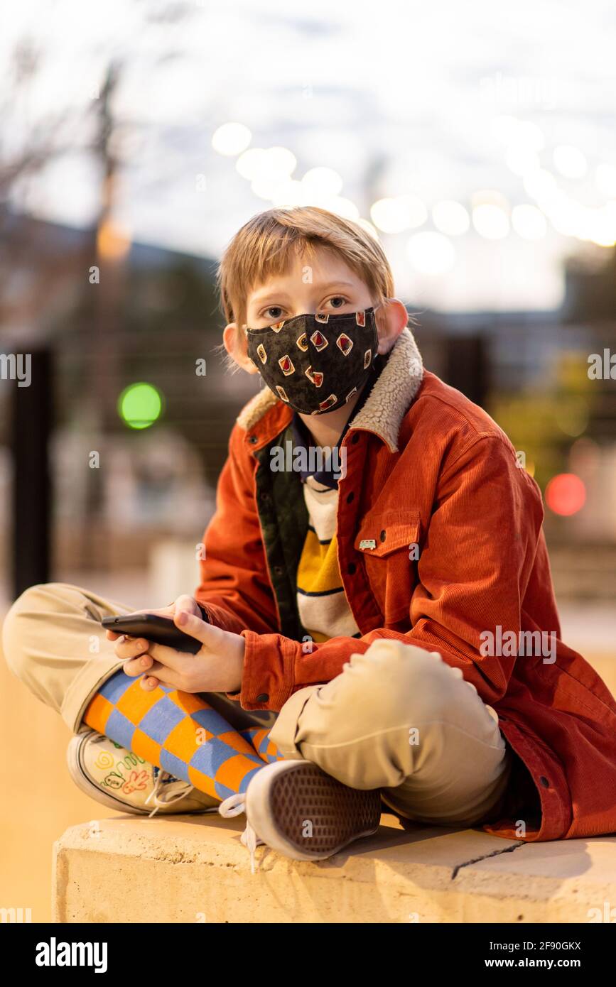 Teenager, der während der globalen Pandemie das Telefon in der Hand hält und eine Maske trägt Stockfoto