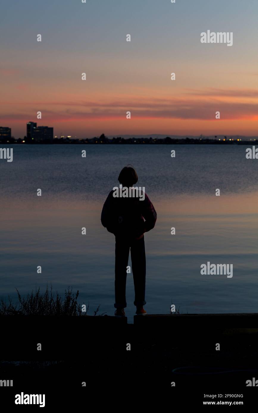 Silhouette einer jungen Person, die während der Zeit über die Bucht auf die Stadt blickt Sonnenuntergang Stockfoto