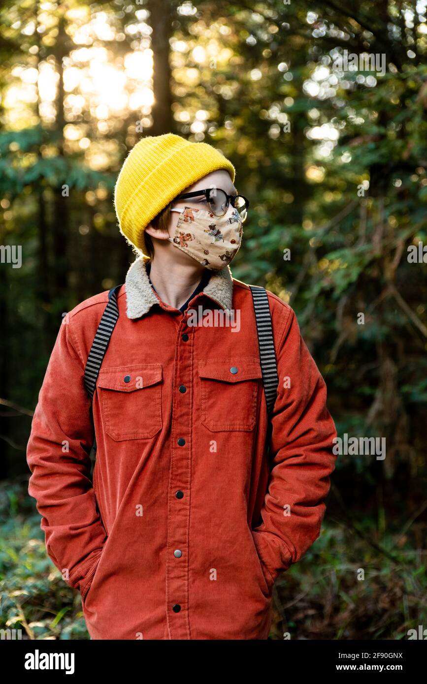 Junge Person, die während einer globalen Pandemie im Wald steht und eine Maske trägt Stockfoto