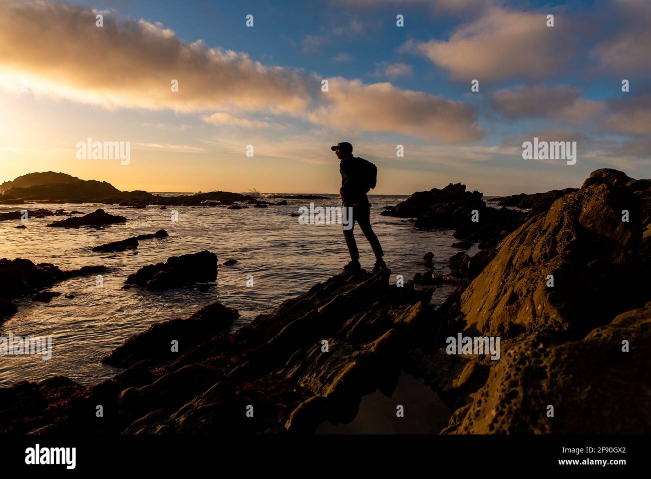 Silhouettenfigur, die am Ufer steht, mit dramatischem Sonnenuntergang am Himmel Stockfoto