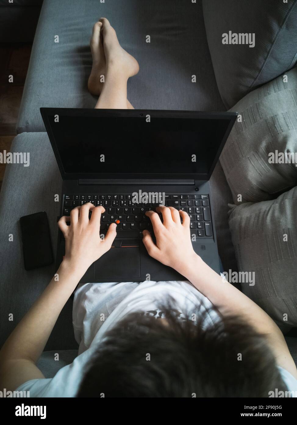 Junge 15 Jahre alt in einem weißen T-Shirt sitzt auf Die Couch mit einem Laptop Stockfoto