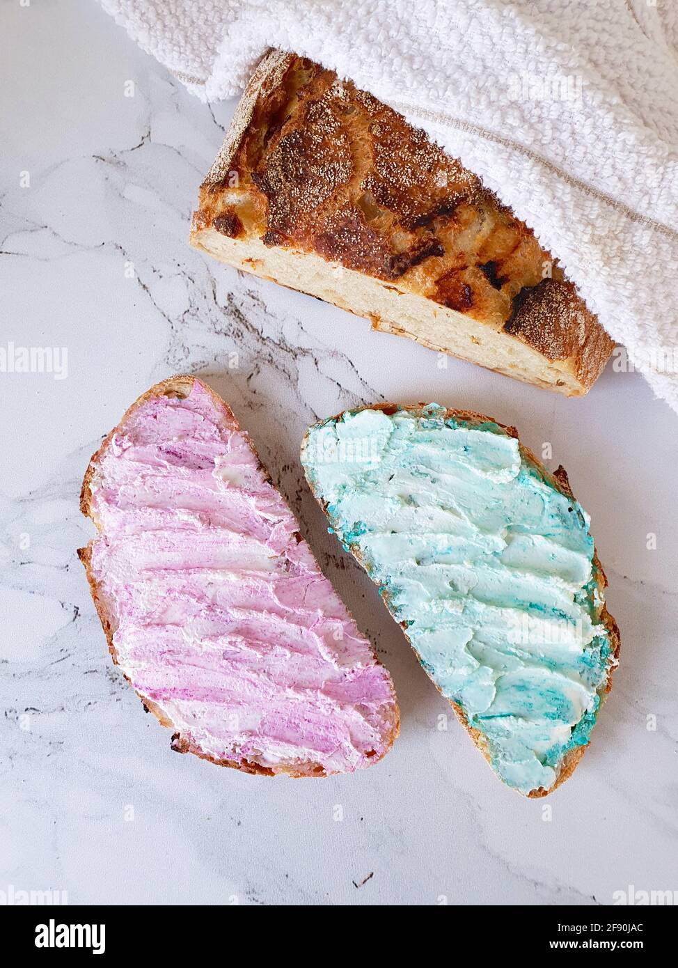 Zwei Brotscheiben mit rosa und blauem Frischkäse Und einem Brotlaib Stockfoto