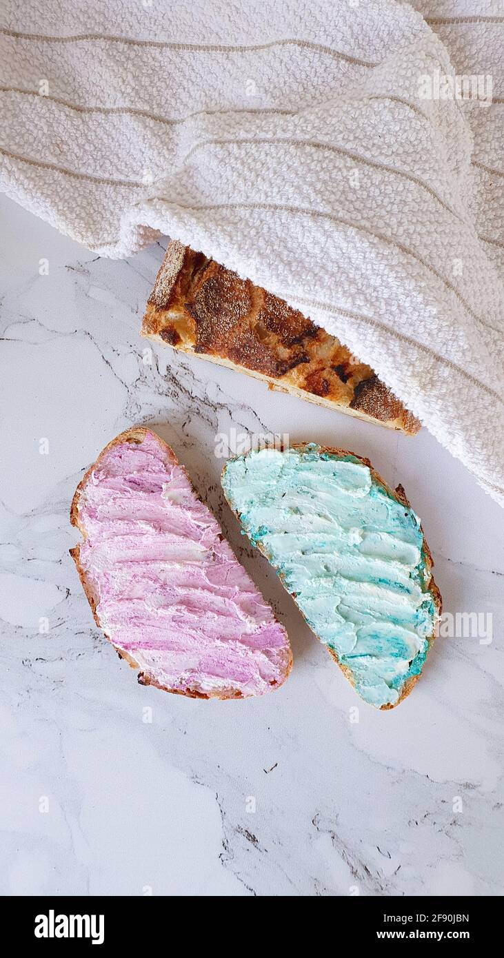 Zwei Brotscheiben mit rosafarbenem und cyanfarbenem Frischkäse Und einem Brotlaib Stockfoto