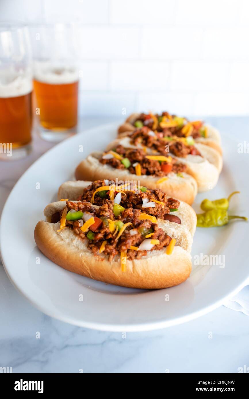 Nahaufnahme eines Tellers mit Chilli-Hunden mit Gläsern Bier im Hintergrund. Stockfoto