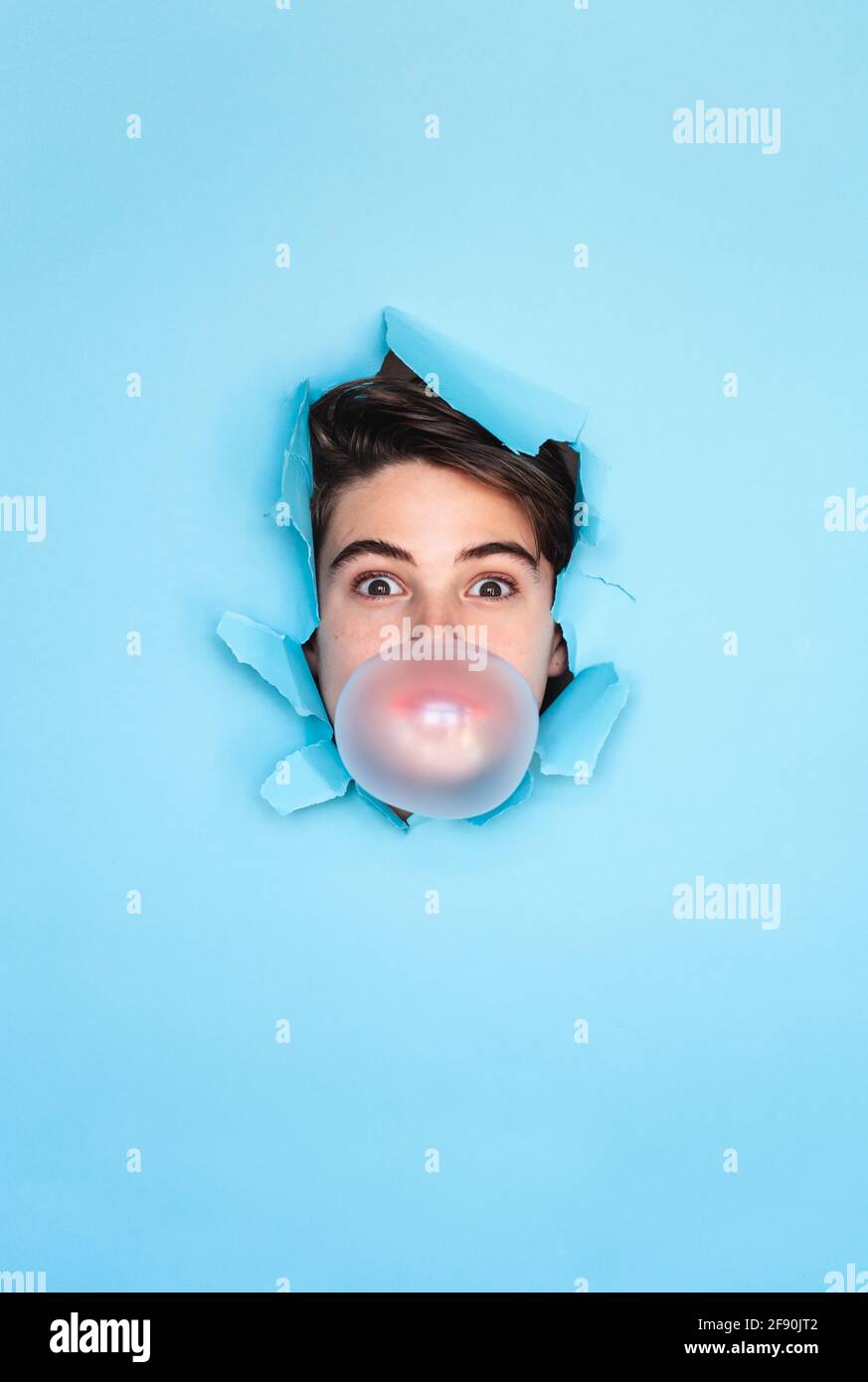 Junge Blase blasen mit Kopf durch Loch in blauem Papier Hintergrund. Stockfoto