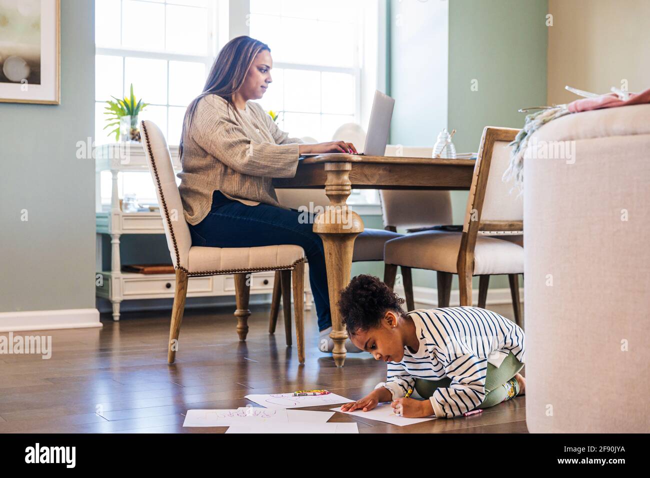 Nettes Mädchen Zeichnung auf Papier, während Mutter mit Laptop, während Sitzen am Tisch im Wohnzimmer Stockfoto