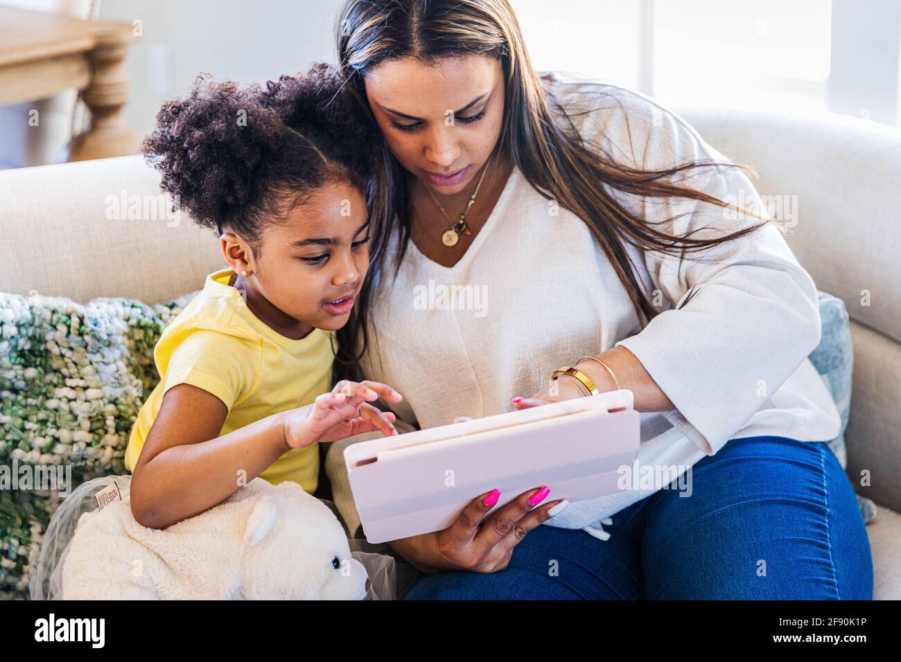 Mutter und Tochter verwenden ein digitales Tablet, während sie auf dem Sofa sitzen Zu Hause Stockfoto