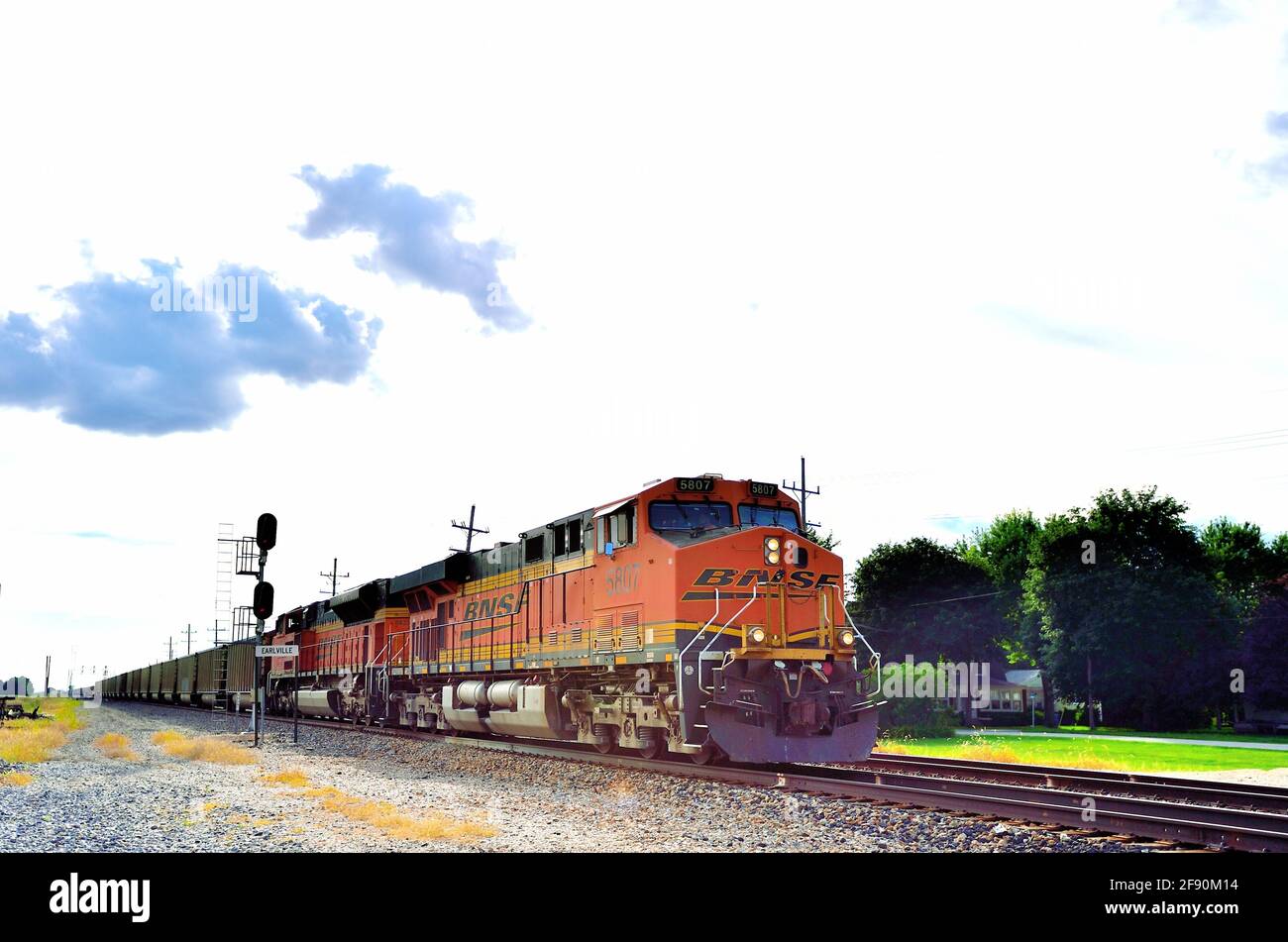 EARLVILLE, Illinois, USA. Ein Zug der Burlington Northern Santa Fe Railway in östlicher Richtung mit leeren Kohlewagen, die durch eine kleine Stadt in Illinois brüllen. Stockfoto