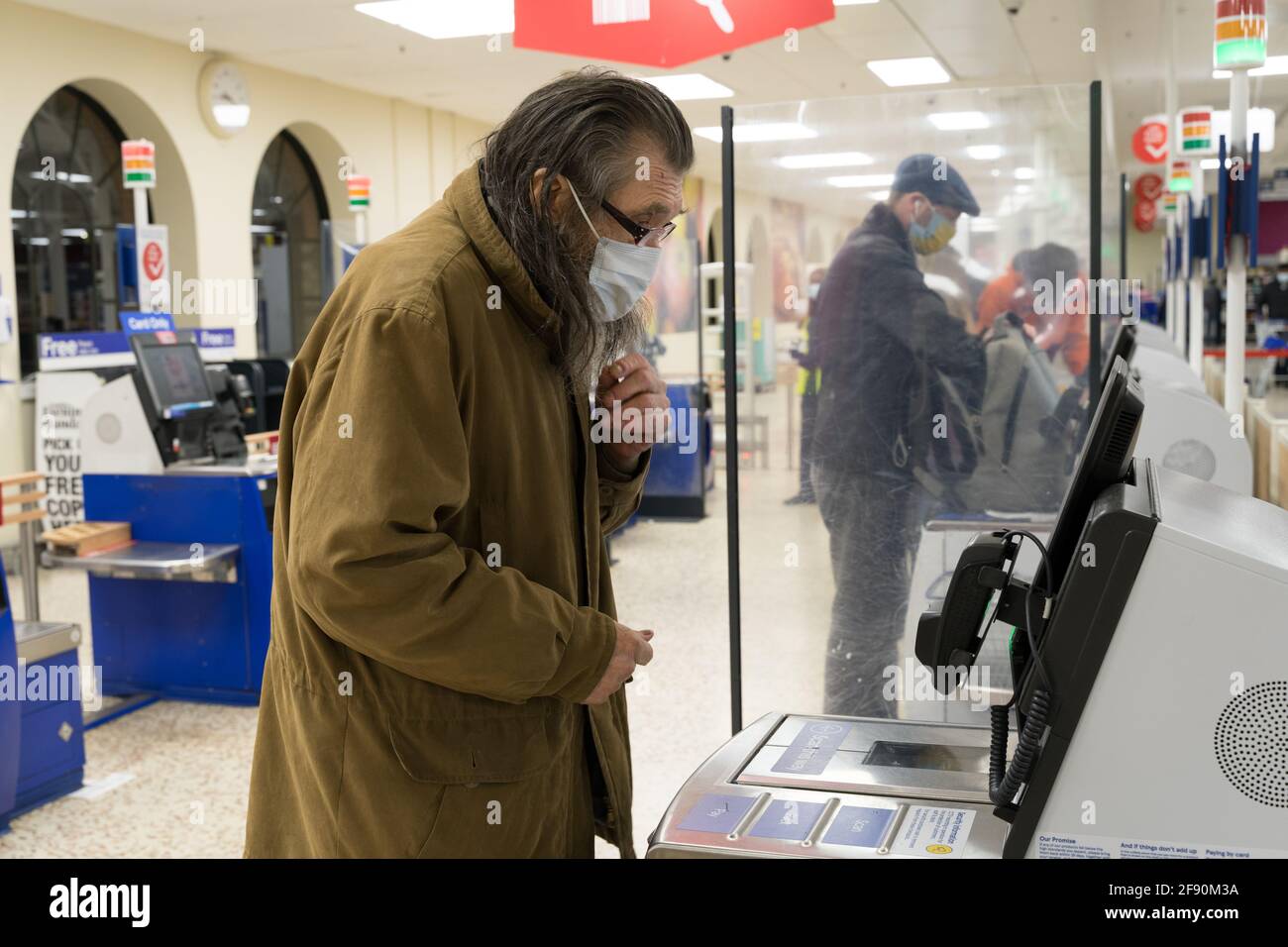 Ein Mann mit Brille, der eine Gesichtsbedeckung trägt, überprüft die Zahlungsoptionen beim Self-Service-Check-out in Tesco, London Stockfoto