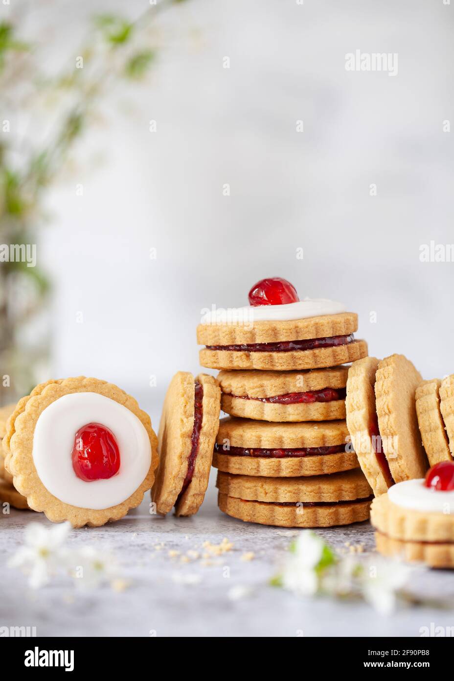 Mit Marmelade gefüllte Shortbread-Kekse stapeln sich, einige mit Glasur und einer Kirsche auf der Oberseite, um Empire-Kekse zu bilden Stockfoto