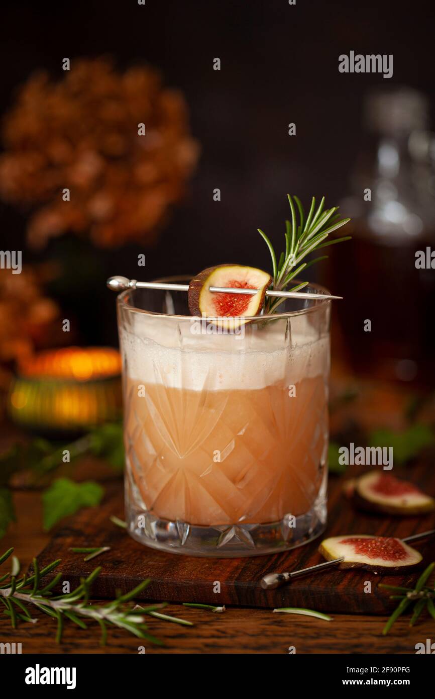 Ein Becher aus Fig Bourbon-Sour-Cocktail mit Eiweiß-Schaum, Feigen- und Rosmaringarnituren Stockfoto