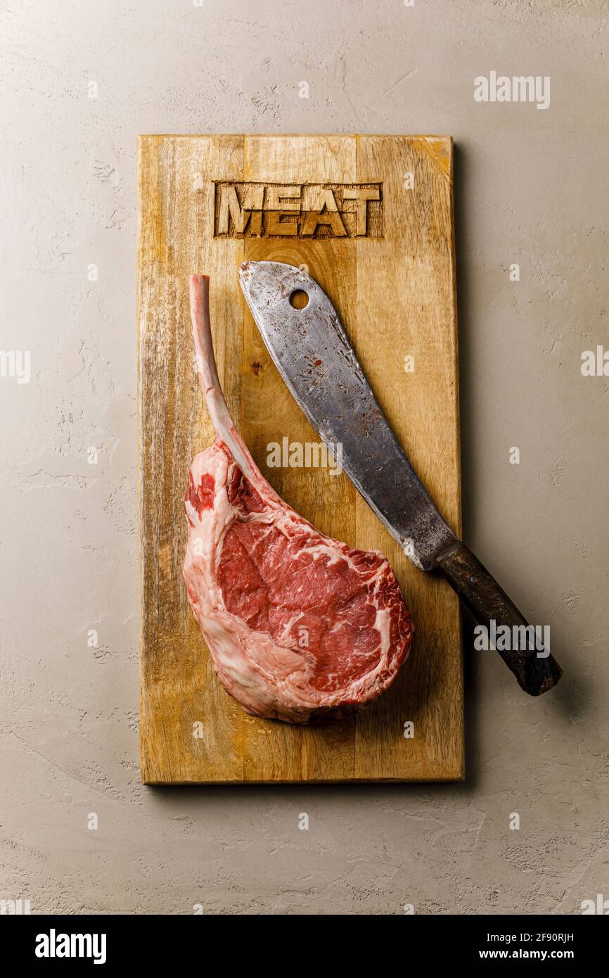 Rohes frisches Fleisch Tomahawk Steak und Metzgerspalter auf Holz Platine Stockfoto