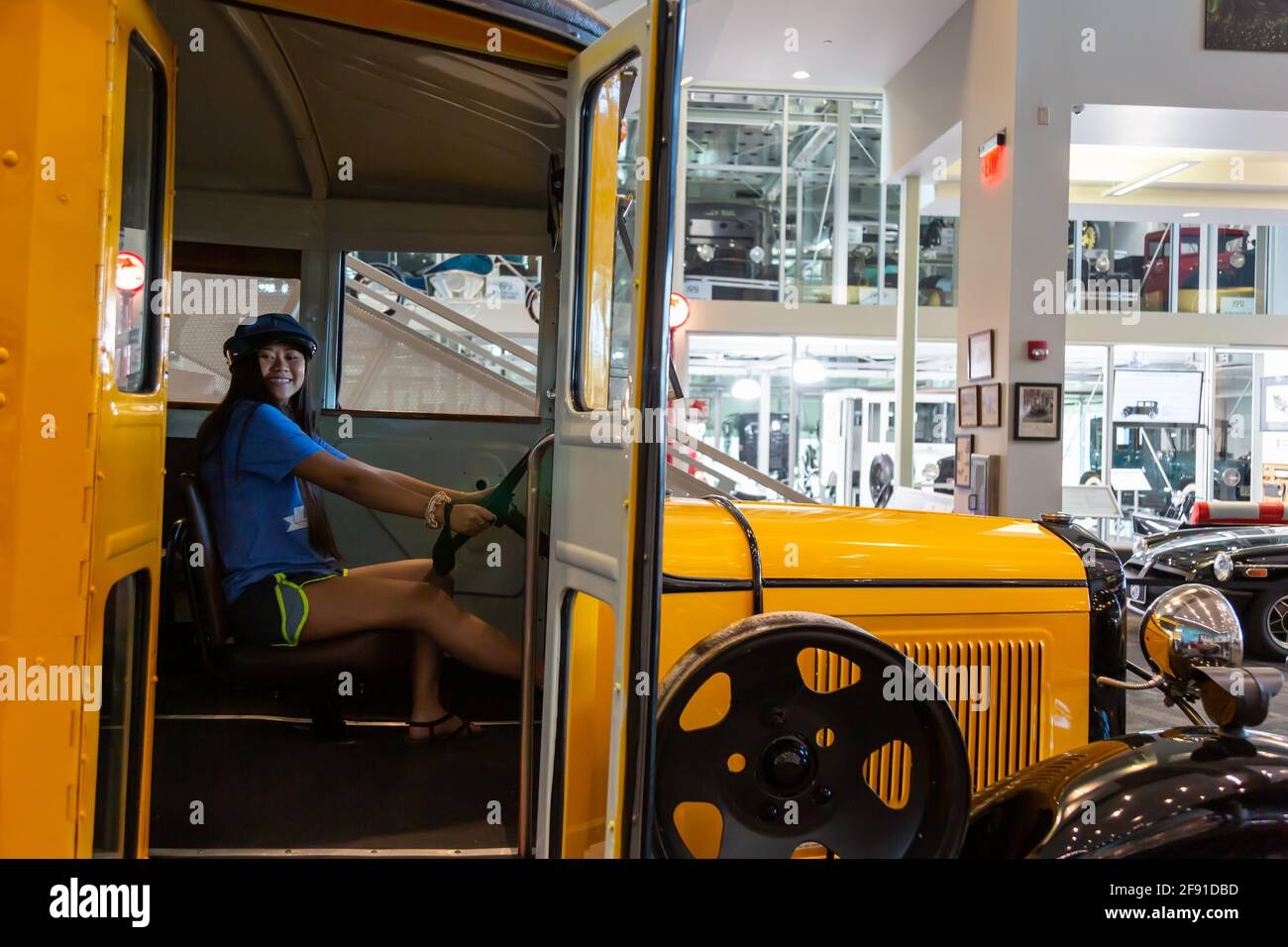 Eine junge Frau sitzt auf dem Fahrersitz eines gelben Ford AA Schulbusses 1931 im Elliott Museum auf der Hutchinson Island in Stuart, Florida, USA. Stockfoto