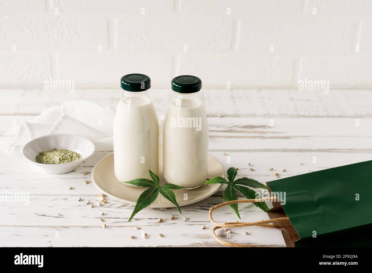 Flaschen mit Cannabis pflanzlichem veganem Gluten und laktosefreier Milch und Cannabisblättern auf Holztisch. Stockfoto