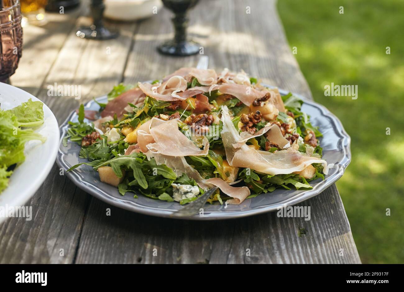Ein wunderbarer Salat aus Rucola, Blauschimmelkäse, Prosciutto, Birne und karamellisierten Nüssen auf einem grauen stilvollen Teller und einem alten Tisch Stockfoto