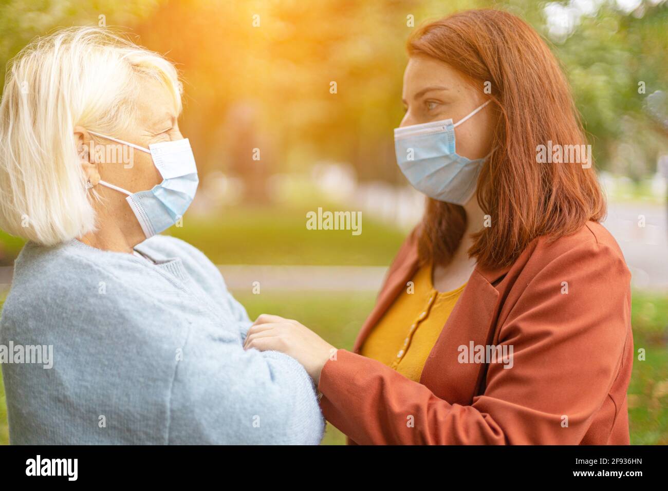 Familienumarmung Mutter und Tochter mit schützenden chirurgischen Gesichtsmasken im Park. Liebe und Freundschaft Konzept. Stockfoto