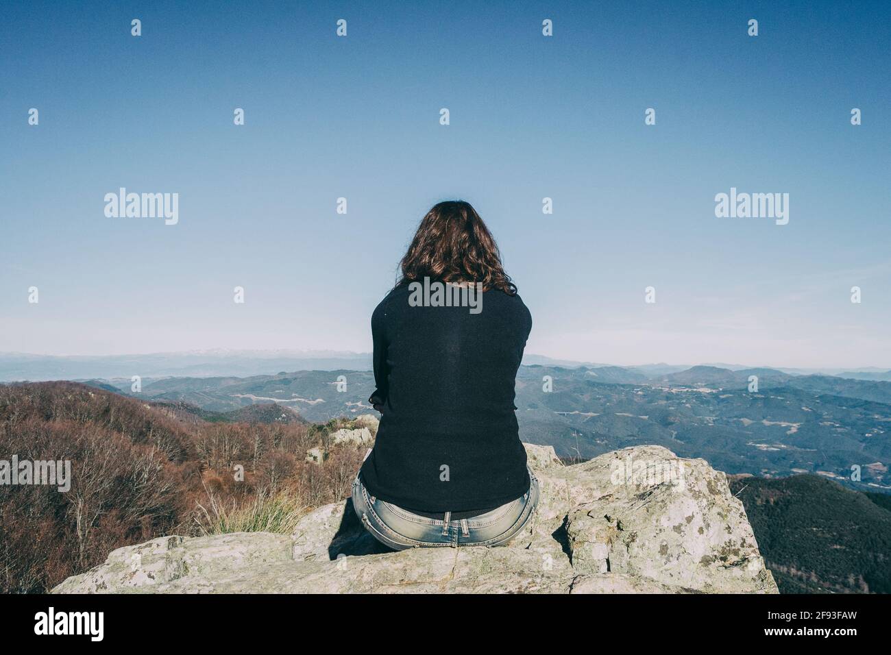 Mädchen von hinten sitzt auf einem Stein oben suchen In den fernen Bergen Stockfoto